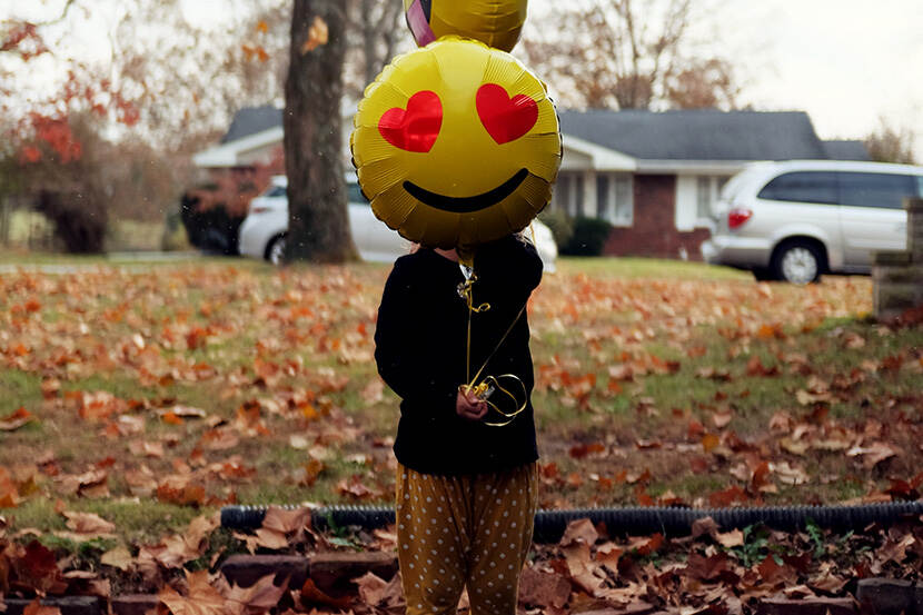 Meisje houdt smileyballon voor haar gezicht.